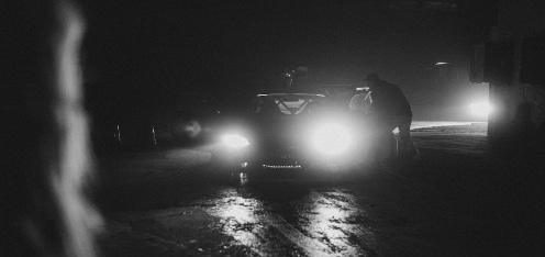 Carro en una vía oscura con las luces encendidas. Imagen a blanco y negro.