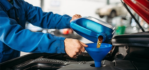 Mecánico de azul cambiando el aceite del motor de un carro rojo.