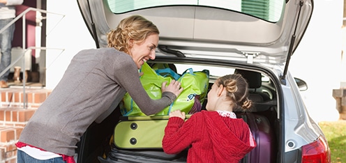 Madre e hija, acomodando maletas en el baúl de un carro.