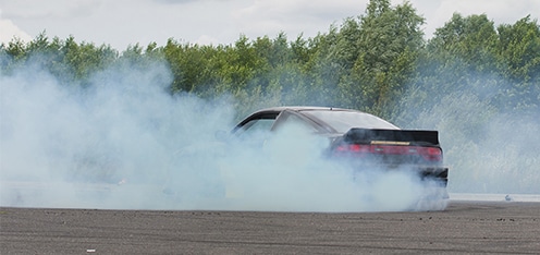 Carro negro en pista, acelerando para generar humo blanco en el carro.